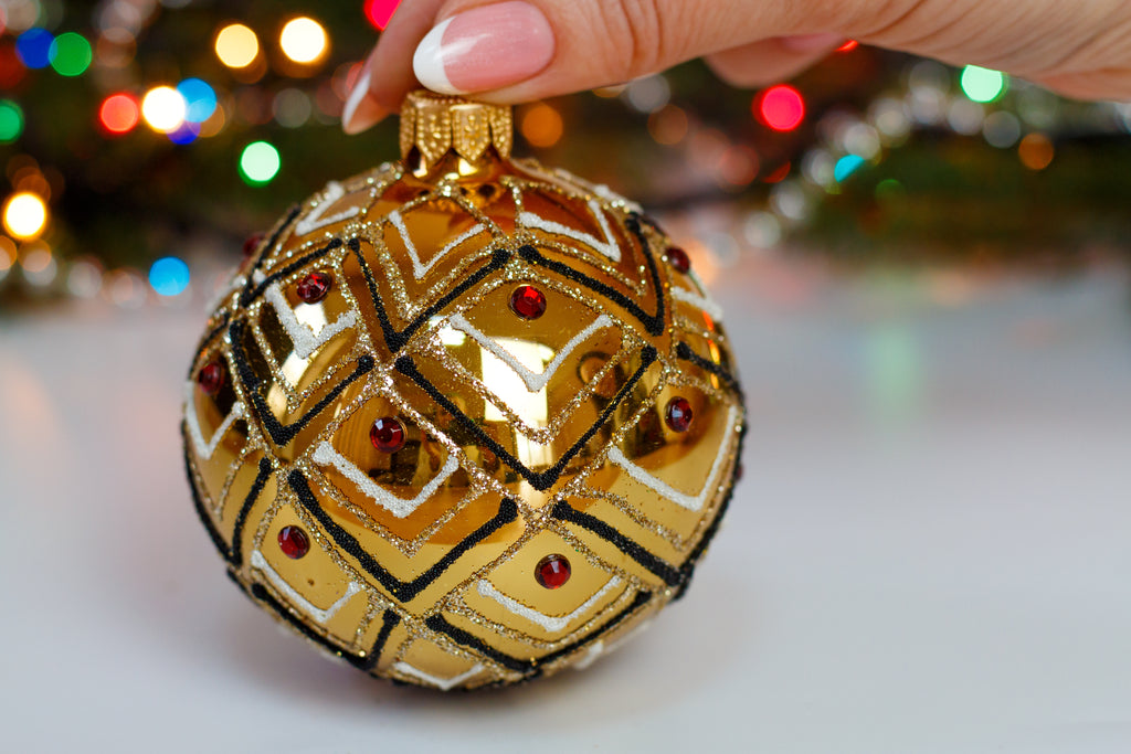 Add a touch of opulence to your Christmas tree with this handcrafted 8 cm gold glass ornament. Designed with a shimmering geometric pattern in black, white, and gold glitter, and adorned with deep red gem accents, this bauble radiates elegance and festive charm. Each piece is delicately blown and decorated by hand in Ukraine, making it a one-of-a-kind heirloom for your holiday collection.

Details:
&nbsp;• Diameter: 8 cm (3.15 inches)
&nbsp;• Material: Hand-blown glass
&nbsp;• Color: Gold with black, white,